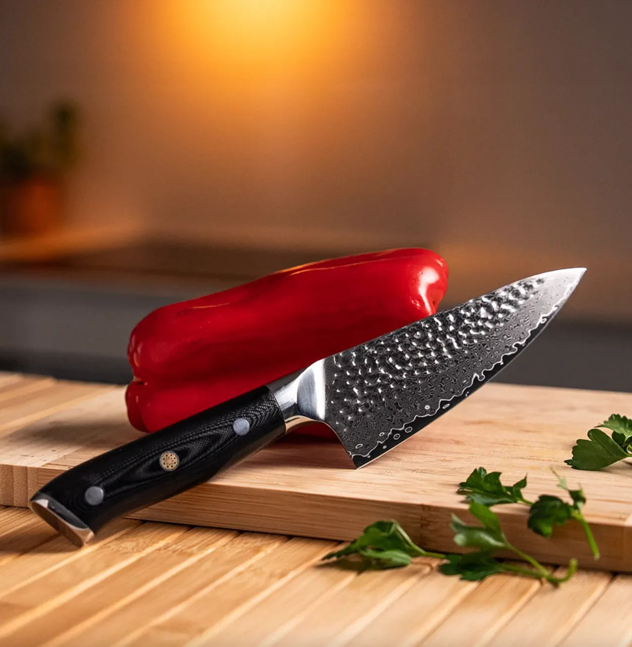 Northern Knife hammered Damascus steel chef knife resting on a bamboo cutting board next to a red bell pepper, featuring a tsuchime finish and ergonomic handle.